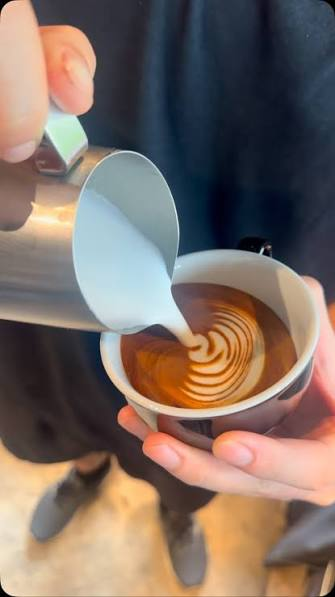 Hands pouring latte art into a ceramic cup at the coffee bar